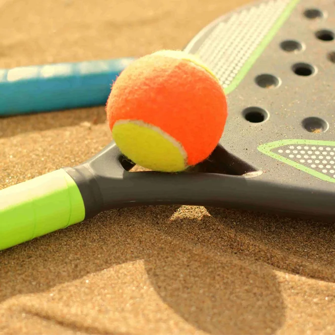 Beach tennis ball beside rackets on sand